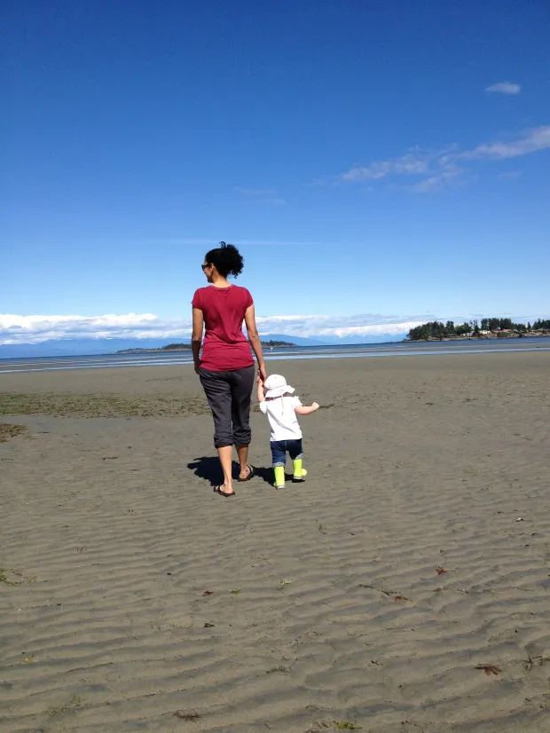 Hand-drawn ink illustration of a woman and small child holding hands on a wide sandy beach under a clear blue sky, warm tan and soft blue tones, calm and hopeful mood